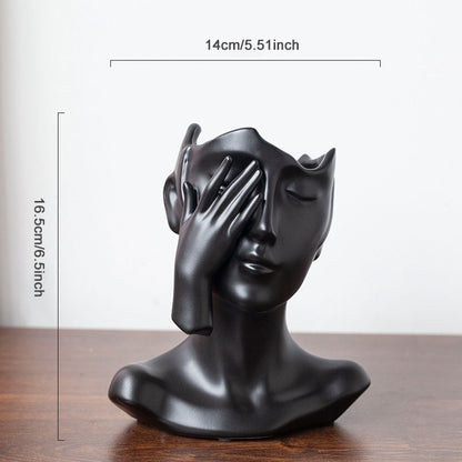 Black sculpture of a face with one hand covering one eye on a wooden surface, with measurements indicated.