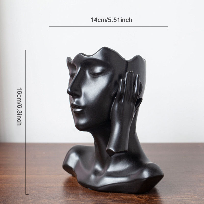 Black sculpture of a woman's head with hand on face on a wooden surface, measurements indicated.