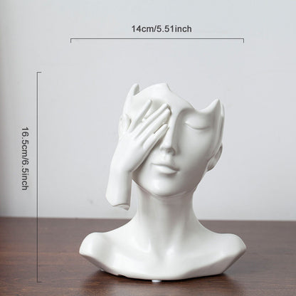 White ceramic bust sculpture with a hand covering one eye, placed on a wooden surface with measurements indicated.