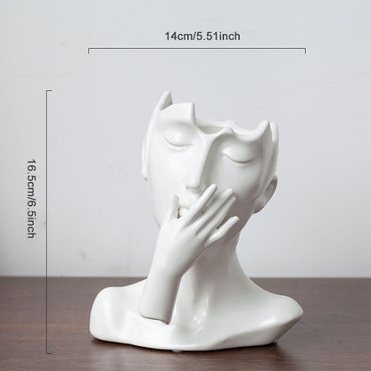 White ceramic sculpture of a face with a hand on a wooden surface, with measurements indicated.