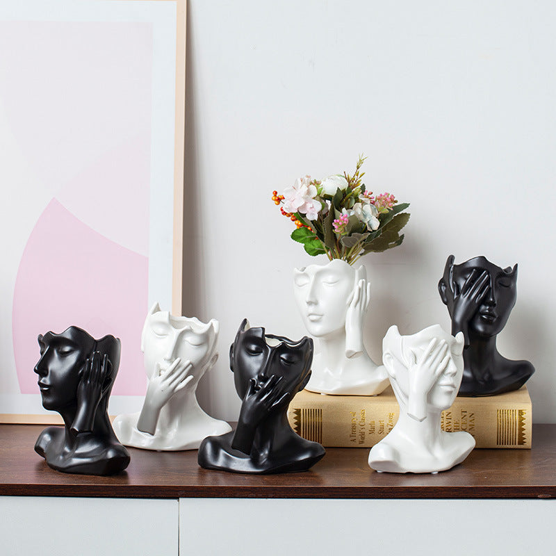 Decorative sculptures of faces on a shelf with a vase of flowers in the background.
