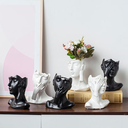 Decorative sculptures of faces on a shelf with a vase of flowers in the background.