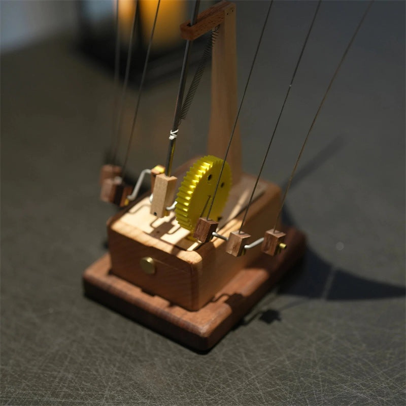 Wooden model of a pulley system with a yellow wheel on a dark surface